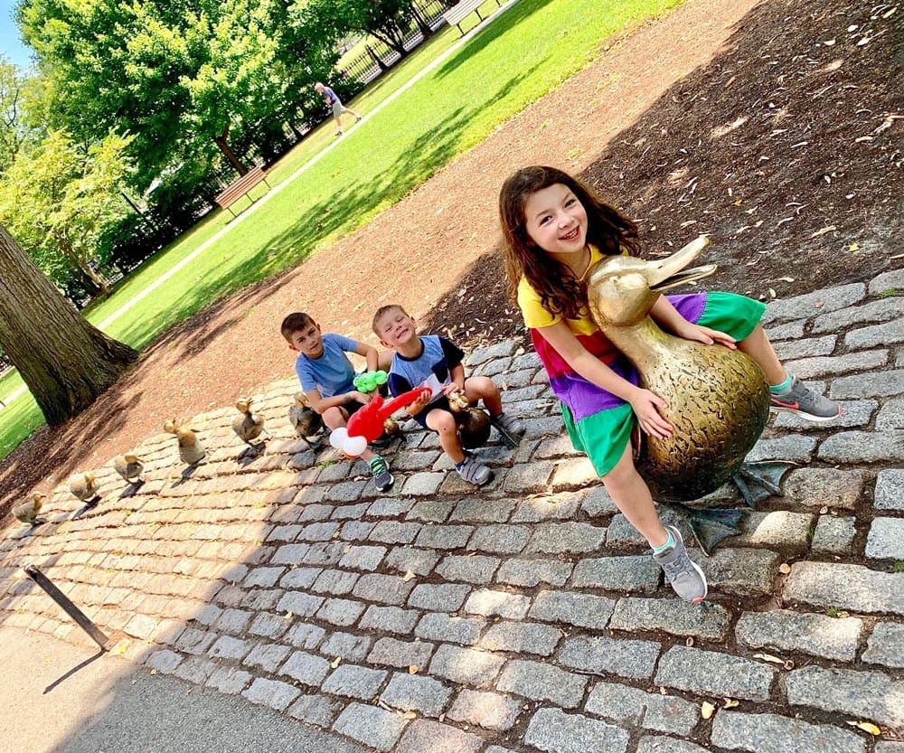 Three kids sit amongst the iconic statue of Ducks in Boston, one of the best Fourth of July destinations for a family trip.