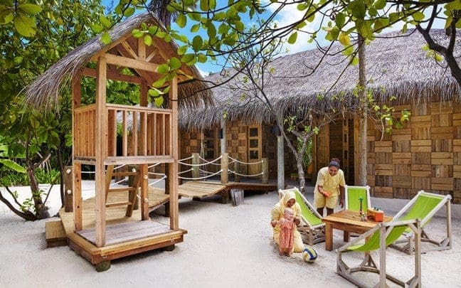 A family sits together near a beach playground at the Six Senses Laamu, one of the best family hotels in the Maldives.