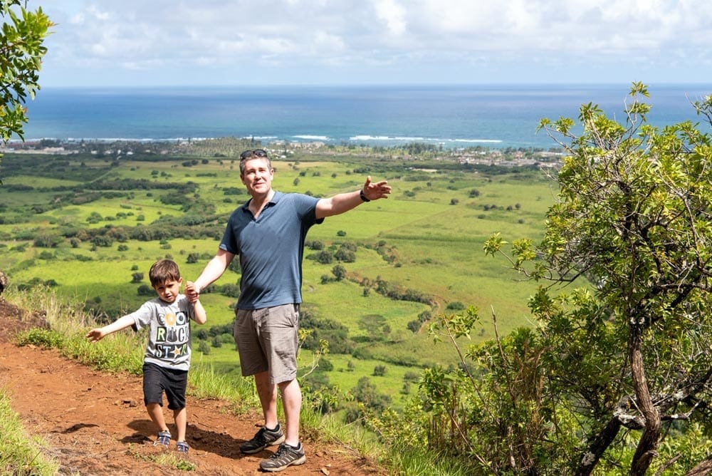 A dad and his young son stand on top of a high hill in Kauai.