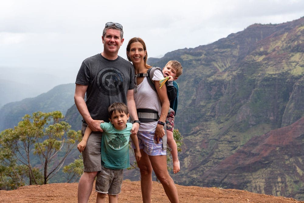 A family of four stand together at the top of a hike in Kauai.