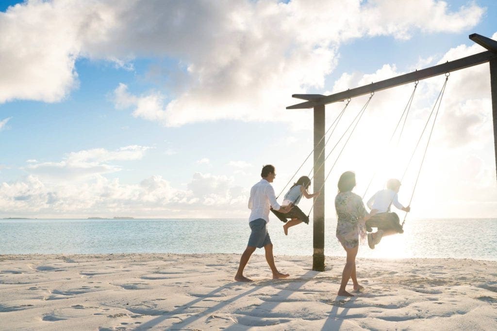 Parents push their two kids on beach swings while staying at the Anantara Dhigu Maldives Resort.