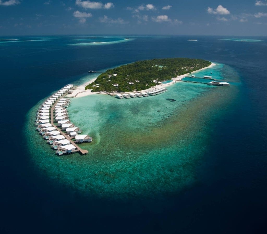 An aerial view of the Amilla Maldives Resort and Residences, featuring a row of over-water bungalows.