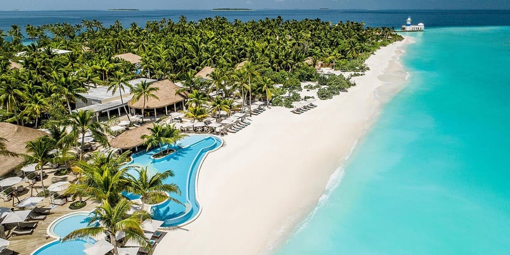 A view of the beachfront property and lush palm trees of InterContinental Maldives Maamunagau Resort, one of the best family hotels in the Maldives.