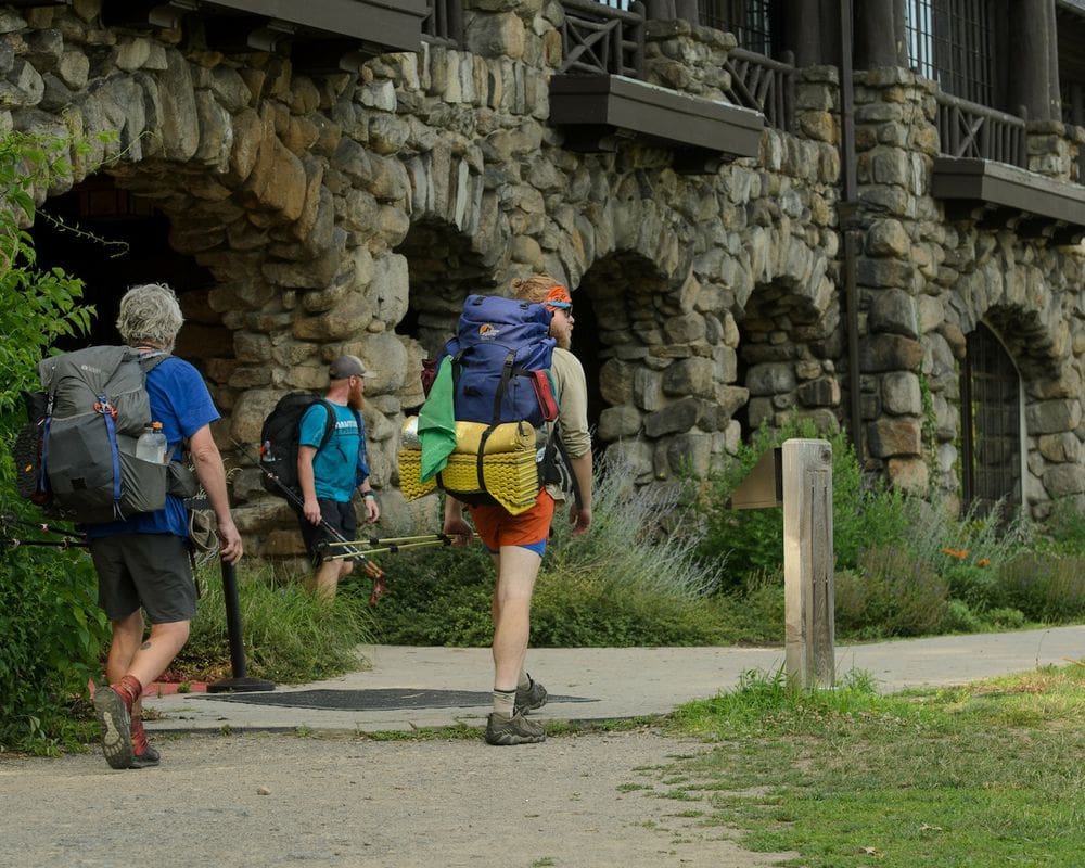 Three men with hiking packs walk outside the Bear Mountain Inn with fishing poles.