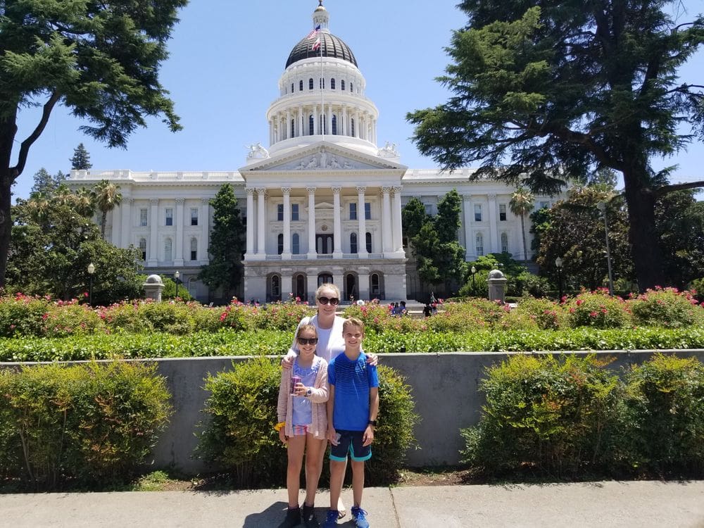 A mom and two of her kids stand in front of the state capitol building in Sacremento.