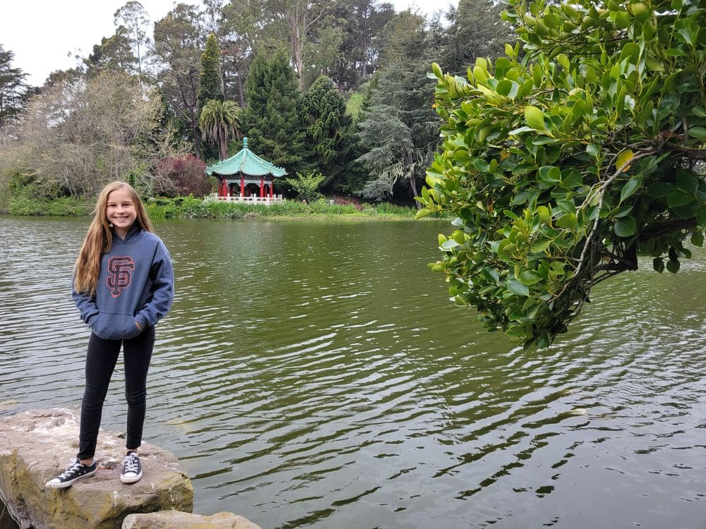 A young girl stands on a rock while exploring an area of Stowe Lake within Golden Gate Park.