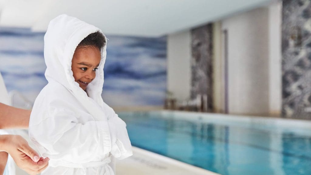 A small child wears a provided kids' bathrobe while looking at the indoor pool at the Four Seasons Hotel New York Downtown.