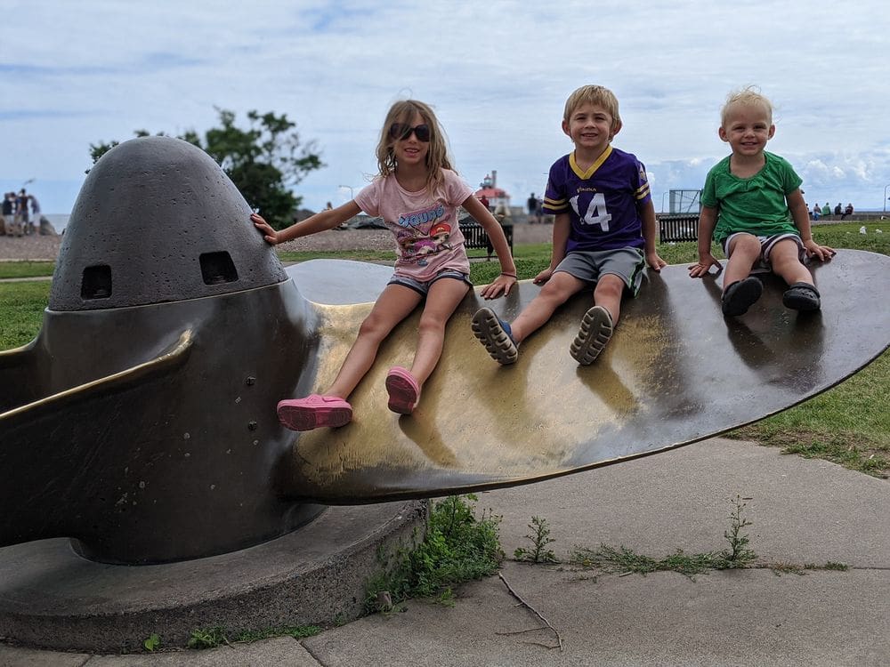 Three kids sit on a large boat propeller that is now an art installation in Canal Park in Duluth, one of the best places to visit northern Minnesota with kids.