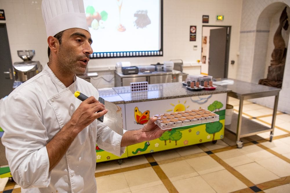 A chef at Choco Story gives a demo to guests, while holding a tray of chocolates.