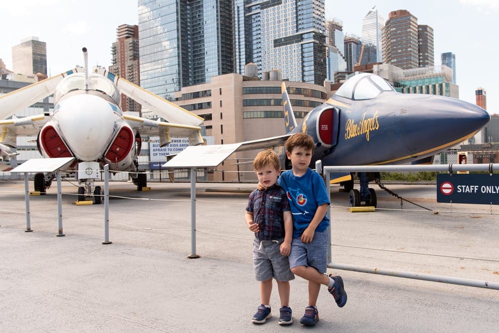 Two boys stand in front of two large planes at the Intrepid Air & Space Museum, one of the best stops on our NYC itinerary with kids.