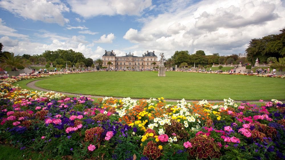 Lucious and colorful gardens surrounding a green area with large buildings in the distance at the Luxembourg Gardens in Paris, one of the best places to visit during Easter with your family.