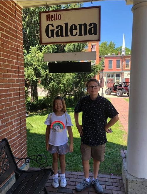 Two kids stand together under a sign reading "Hello Galena".