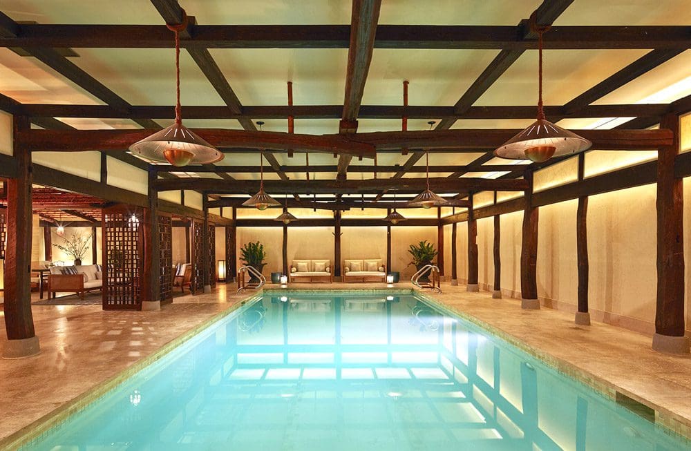 A view of the indoor pool at the The Greenwich Hotel, with nearby loungers and well-designed space featuring wood beams at one of the best family hotels in New York with pools.