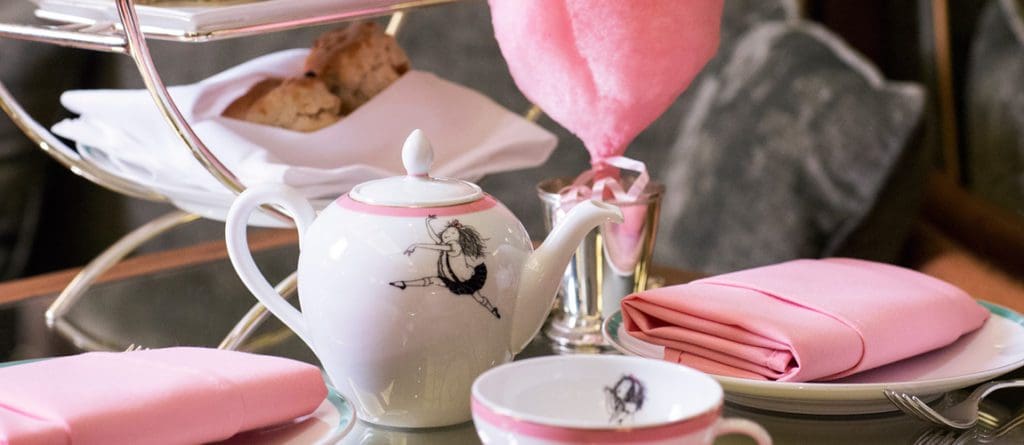 A tea cup and pot, surrounded by pink napkins, rest on a table during the Eloise At The Plaza afternoon tea.