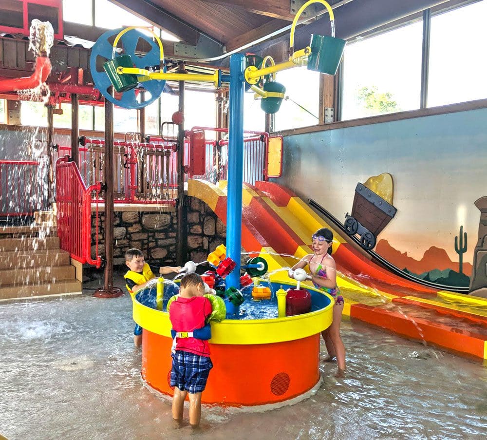 Four kids play at a water table, part of the indoor water park at Big Splash Indoor Water Park and Boulder Bay Outdoor Aquatic Adventure at Rocking Horse Ranch Resort.