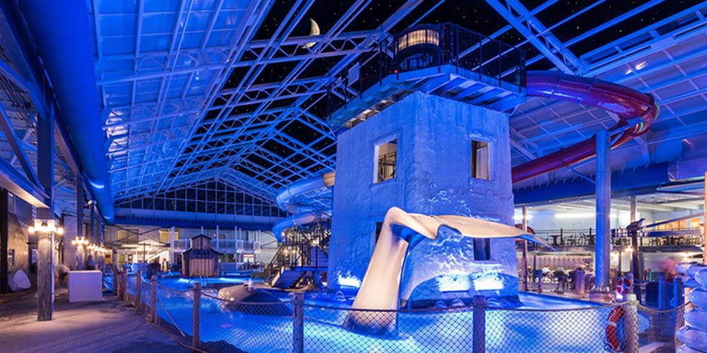 Inside the blue-lit indoor waterpark at Cape Codder Water Park at Cape Codder Family Resort and Spa, featuring a large whale tail and lighthouse tower.