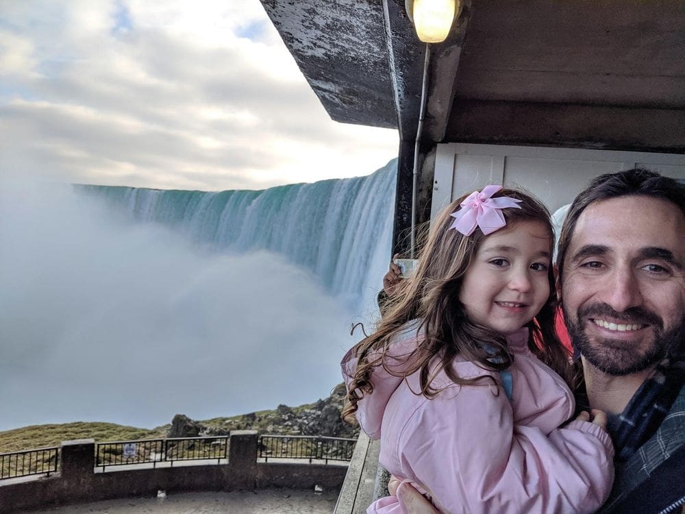 Father and daughter smile with a view of Niagara Falls behind them as they await the Journey Behind the Falls Tour.