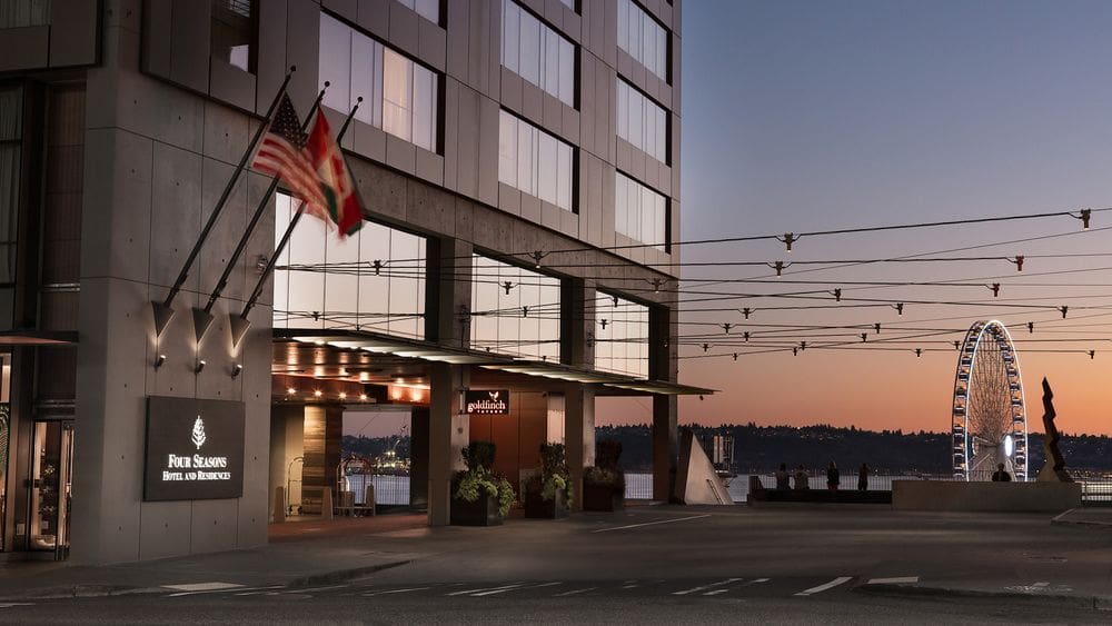 The exterior of Four Seasons Hotel Seattle, in the distance is the waterfront and iconic Seattle Ferris wheel.