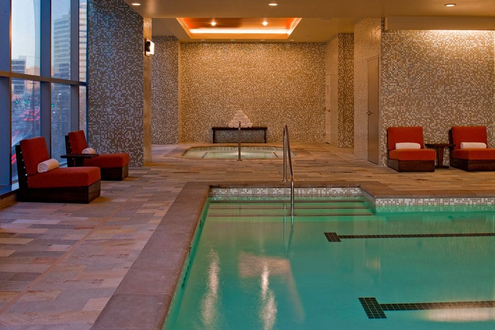 Inside the spa pool area at Hyatt at Olive 8, featuring a large pool, hot tub, and red poolside loungers.