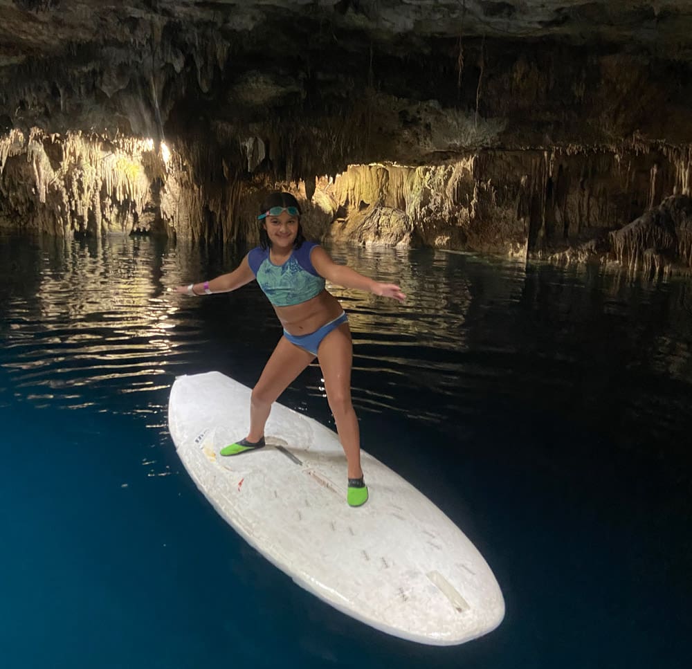 A young girl stands on a paddleboard while enjoying Cenote Kin Ha.