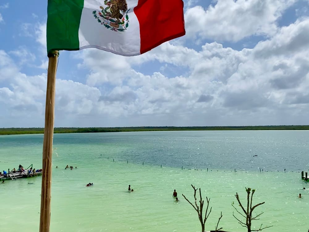 A Mexican flag flies high above a shoreline near Laguna Kaan Luum, one of the best day trips from Playa del Carmen for families.