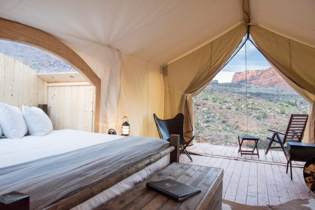 Inside a glamping safari tent at Under Canvas Zion, featuring a large bed and chair with a view of the desert beyond.