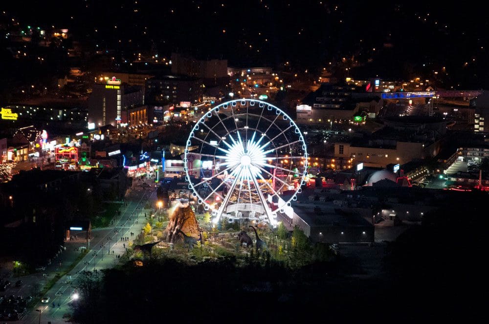 An aerial view of the Niagara Skywheel at night lit-up with city lights behind it.