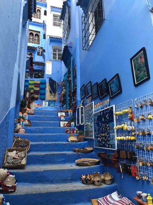 An alley stairway is painted blue and covered with colorful baskets and wares in Chefchaouen, Morocco.