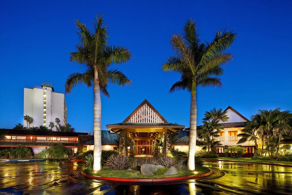 The entrance to the Catamaran Resort Hotel and Spa, flanked by two large palm trees, at night, one of the best San Diego beachfront hotels for families.