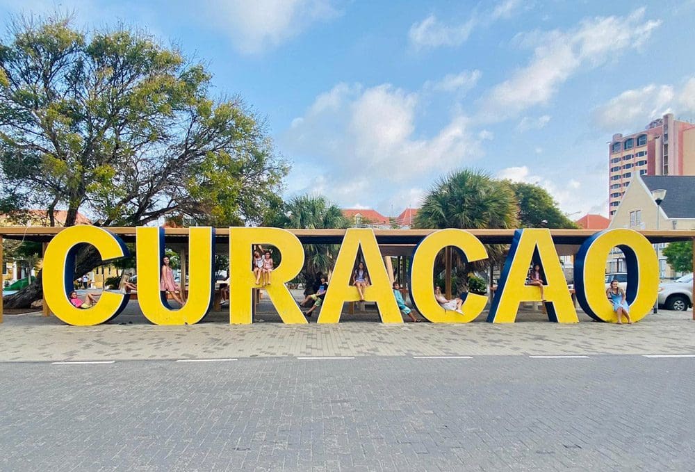 Several kids sit amongst a large statue spelling our Curacao in yellow.