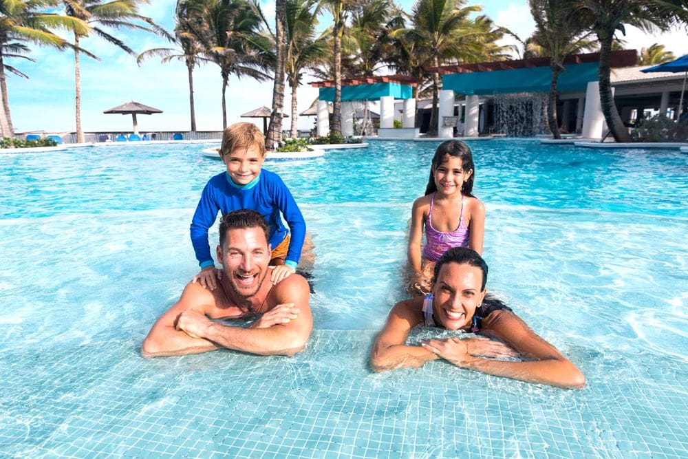 A mom, dad, and two kids pose together in a pool at the Coconut Bay Beach Resort & Spa.