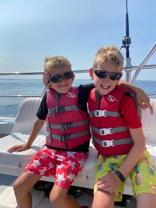 Two boys, both wearing red life jackets, sit together while enjoying a whale watching cruise.