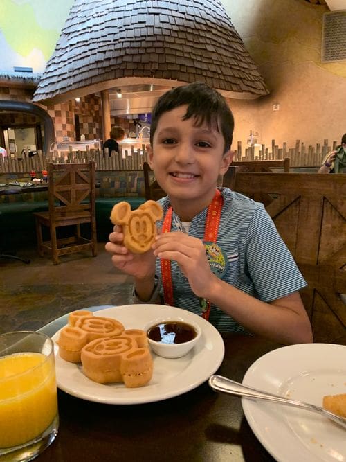 A young boy holds up a Mickey-shaped waffle while enjoying breakfast at the Animal Kingdom Lodge.
