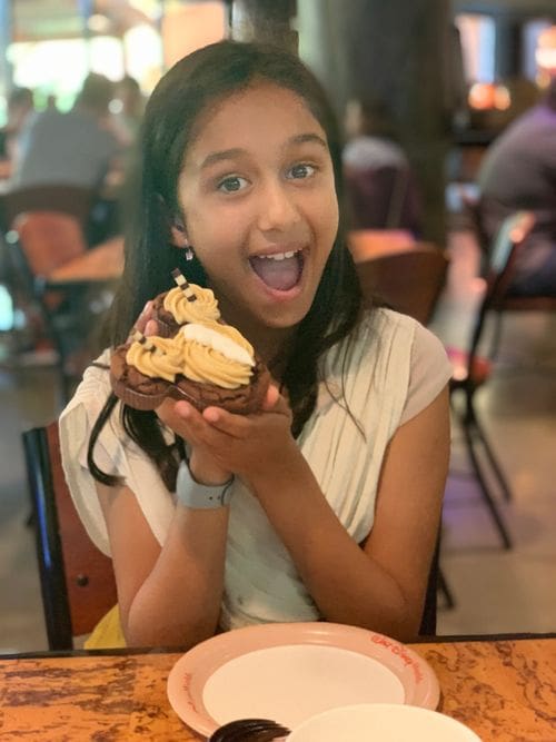 A young girl holds up a Mickey Mouse-shaped dessert while enjoying a meal at the Animal Kingdom Lodge, a great Disney Deluxe Resort for families.
