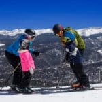 A family of four poses together in full ski gear while enjoying the slopes in front of Grand Lodge on Peak 7.
