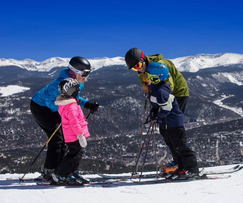 A family of four poses together in full ski gear while enjoying the slopes in front of Grand Lodge on Peak 7.