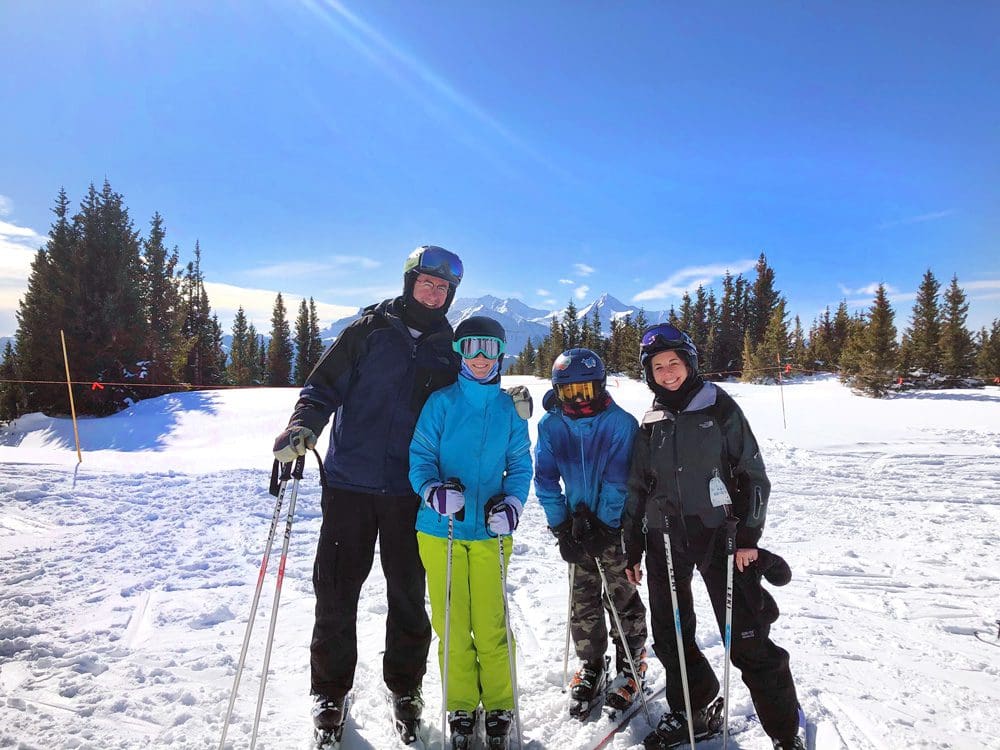 A family of four poses together in full ski gear while enjoying the slopes at Telluride, one of the best vacation spots in the US to impress teens and tweens.
