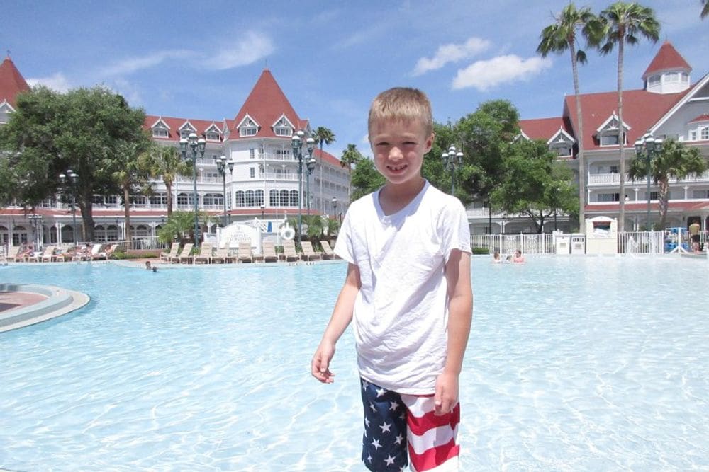 A young boy wearing American flag swim shorts stands in the pool at the Grand Floridian Resort, a great Disney Deluxe Resort for families.