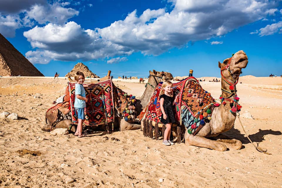 Two kids stand near respective camels awaiting a tour in Egypt.