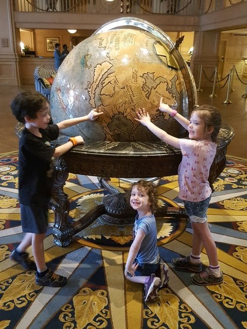 Three kids excitedly point on a globe within the lobby of the Disney Yacht Club, a great Disney Deluxe Resort for families.