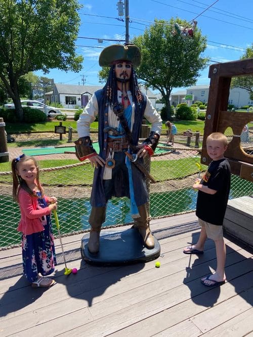 Two kids stand with a carved, wooden pirate while playing mini golf in Cape Cod.