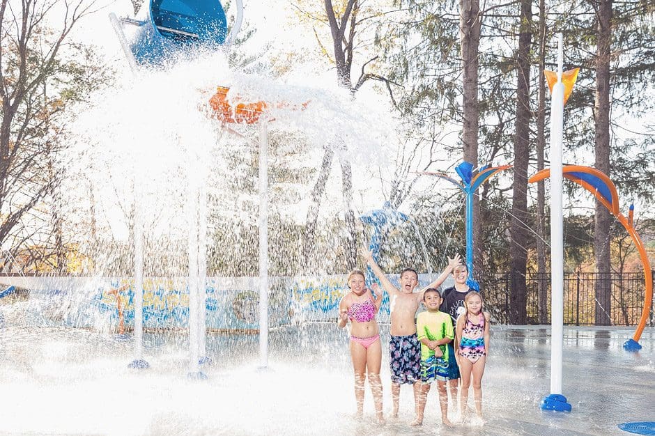 Five kids stand together laughing while enjoying a large splash pad water feature at the Odetah Camping Resort, one of the most family-friendly hotels in Connecticut.