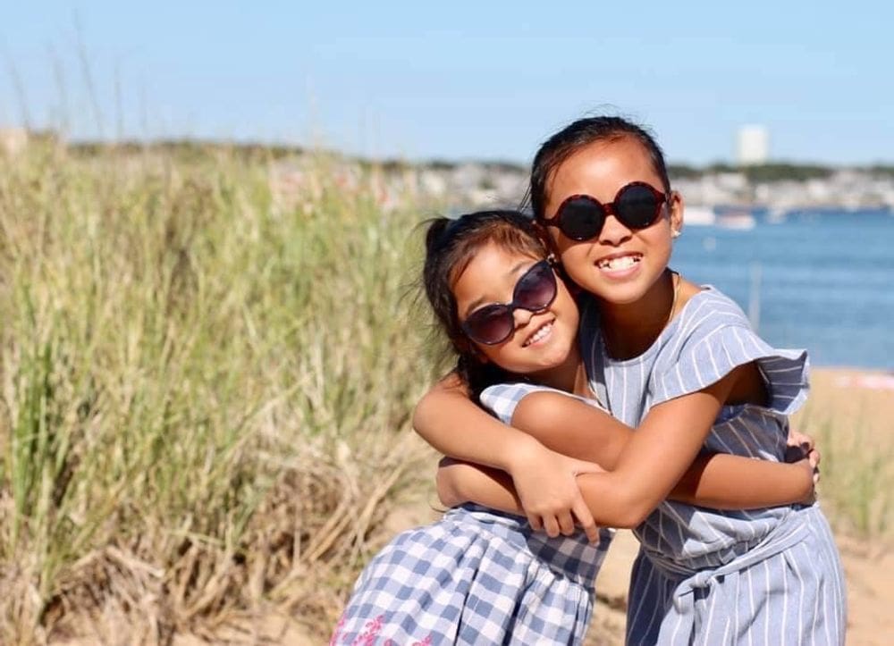 Two sisters wearing lovely dresses hug one another while enjoying a sunny day on the beach in Cape Cod.