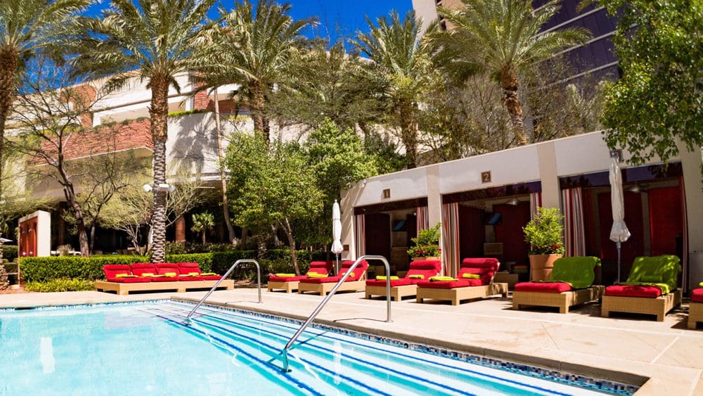 A close-up of the outdoor pool at the Red Rock Casino Resort and Spa, with red pool loungers on the other side of the pool.