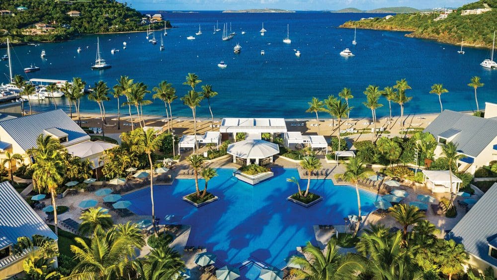 An aerial view of the pool and lush grounds at the The Westin St. John Resort Villas, with the marina full of ships in the distance.