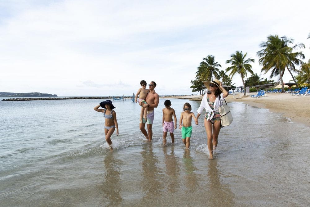 A family of six walks together along the shallow waves at the Windjammer Landing Villa Beach Resort.