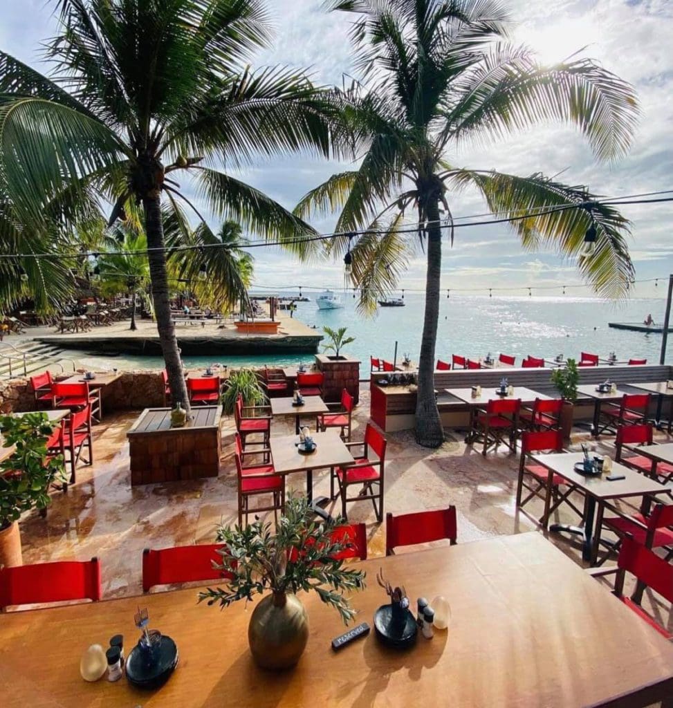 Tables and chairs waiting for guests on the beach at Zanzibar Restaurant & Bar, with swaying palm trees in the distance.
