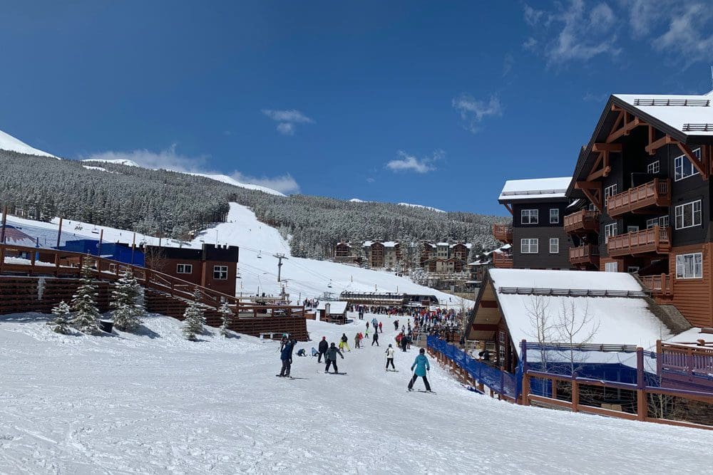 Families mill about Breckenridge Ski Resort on a sunny winter day.