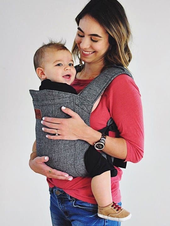 A mother holds her infant in a charcoal Happy Baby Carrier on her front.