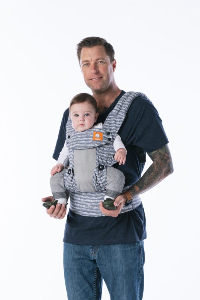 A man holds his child in a front carrier by Tula Coast Explore Mesh Baby Carrier.